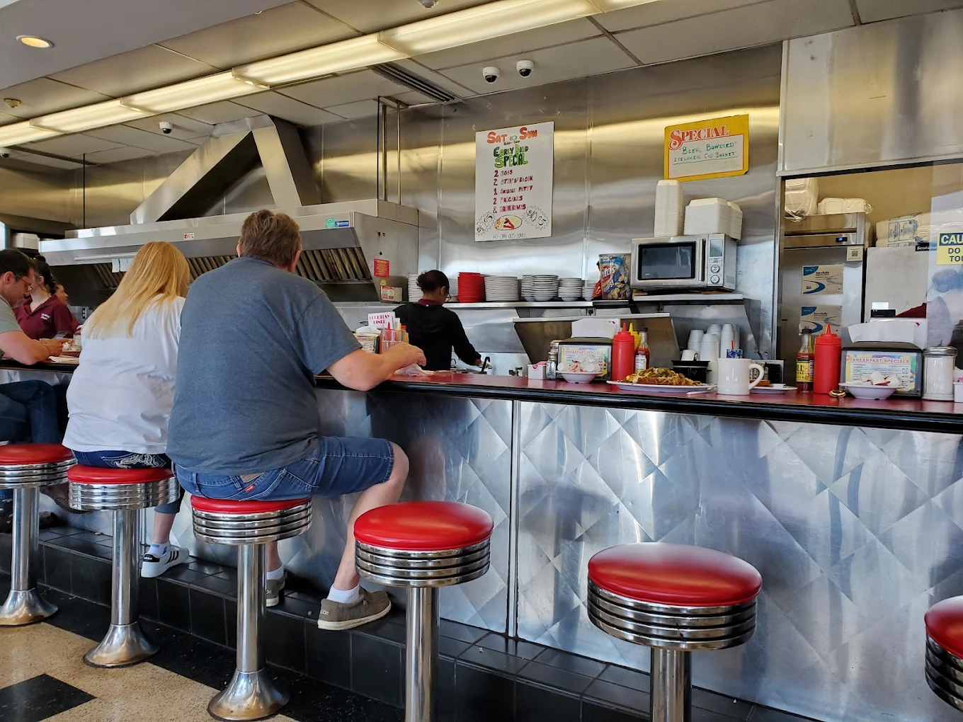 Courtesy Diner counter with red stools, chrome trim, and guests along the rail.